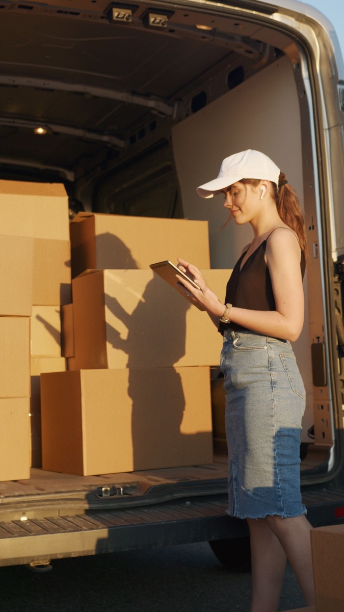 Courier organising deliveries beside an open van during low evening light.